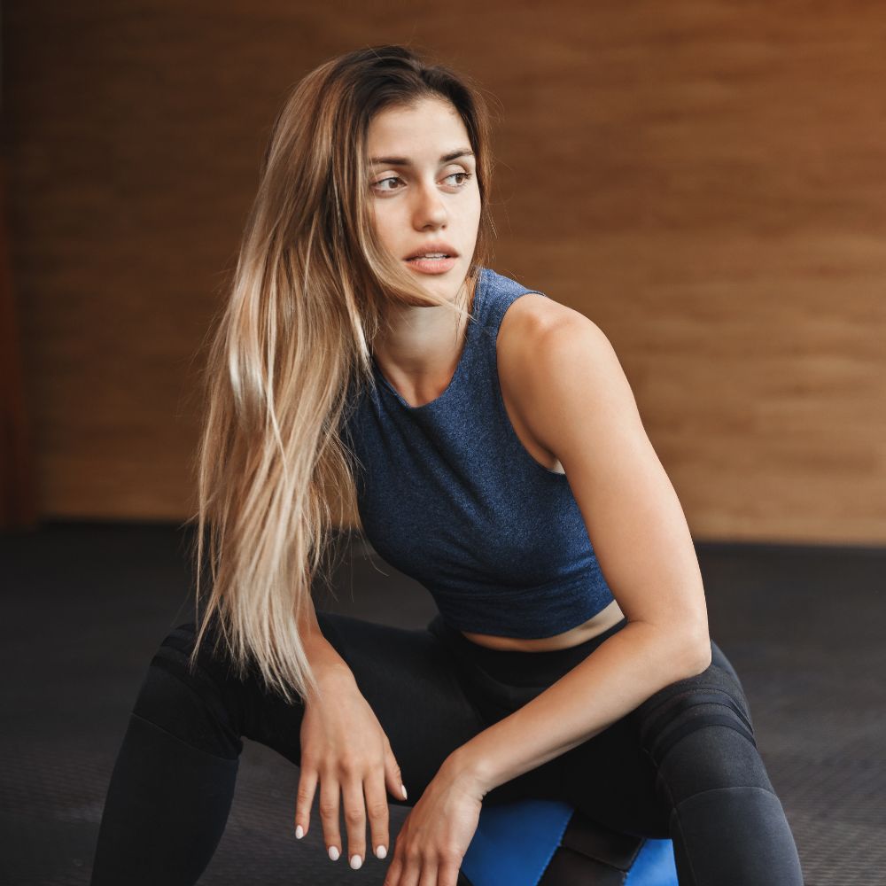 Woman in athletic wear sitting on a blue exercise ball against a wooden wall.